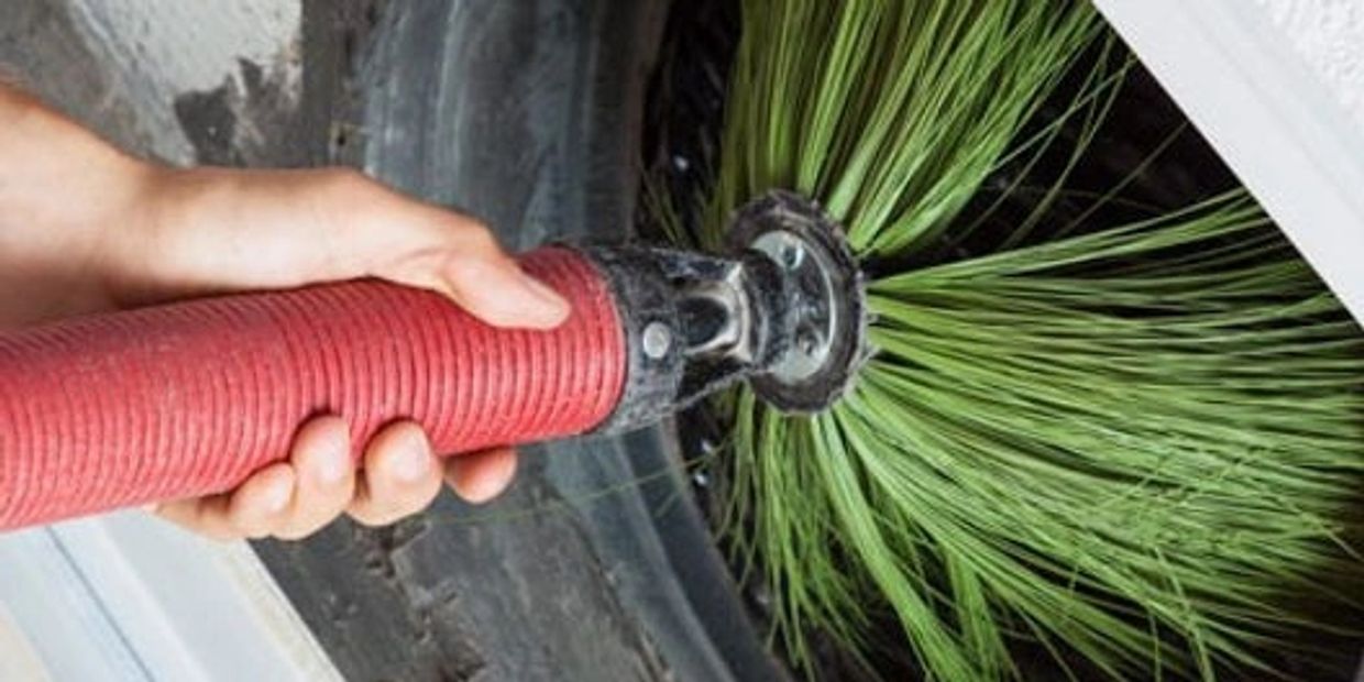 Hand holding a red hose with green brush cleaning a pipe.