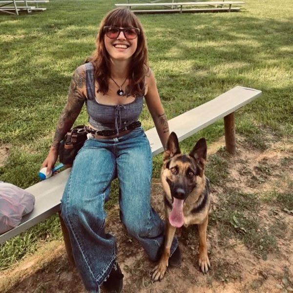 Smiling woman sitting on a bench outdoors with a happy German Shepherd dog.