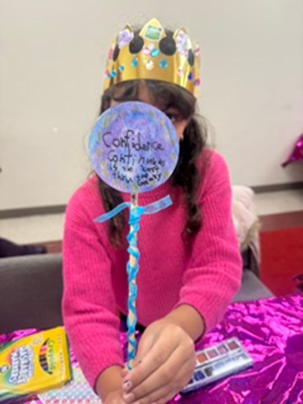 Child with crown holding a decorated craft stick.