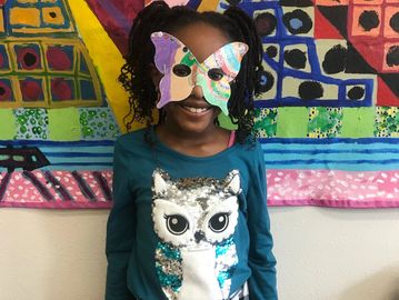 Child wearing a butterfly mask and an owl shirt.