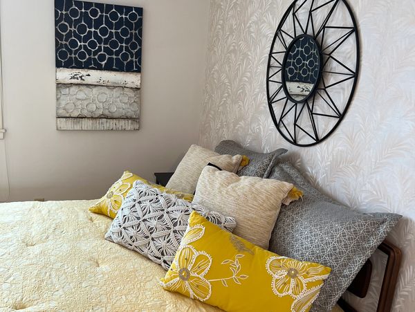 A cozy bed with yellow and gray decorative pillows, a textured quilt, and modern wall art. Porchlight Home Staging by Sheila Fritts 