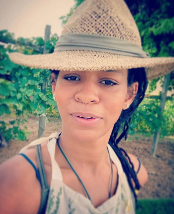 Woman wearing a straw hat and apron outdoors in a garden or vineyard.