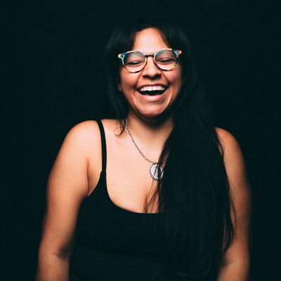 Woman with glasses laughing joyfully against a dark background.