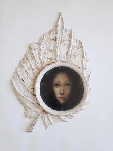 A portrait of a woman framed in a textured leaf-shaped frame.