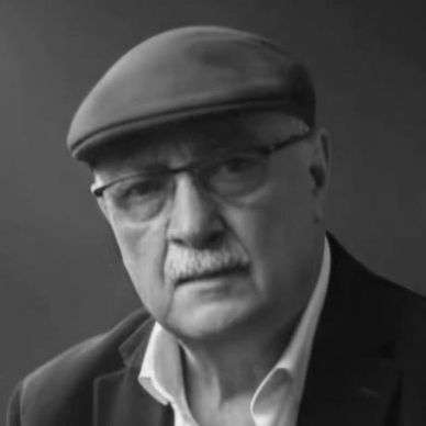 Black and white portrait of an elderly man wearing glasses and a flat cap.