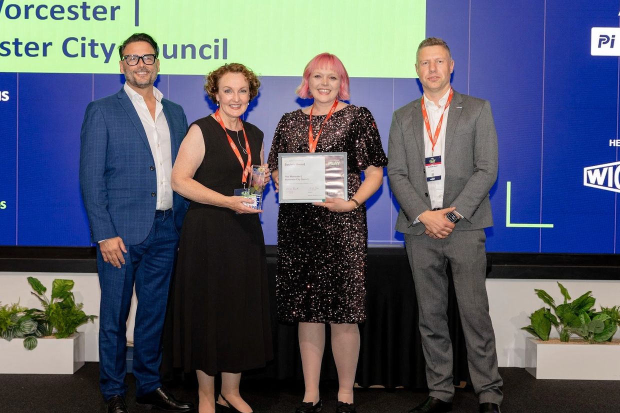 4 adults stood on a stage. Two women in the middle receiving an award.