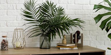 a desk with palm leaves against a white brick wall