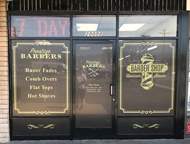 Barber shop front with gold lettering advertising services like razor fades and hot shaves.