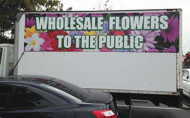 Truck with a sign offering wholesale flowers to the public.