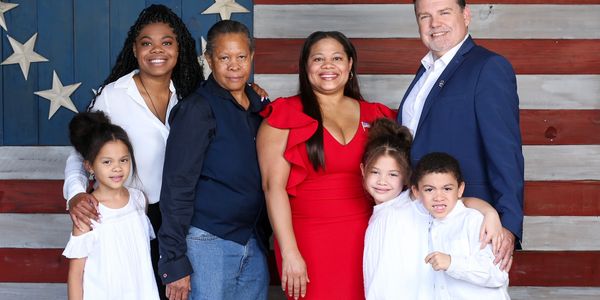 A diverse family posing in front of an American flag backdrop.