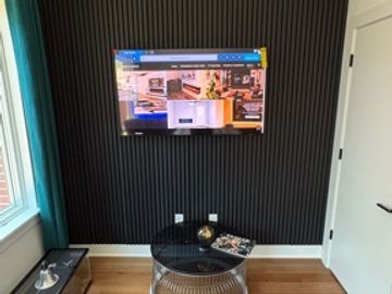 Black acoustic-panel TV wall with hidden wiring installed by MASS Studios.