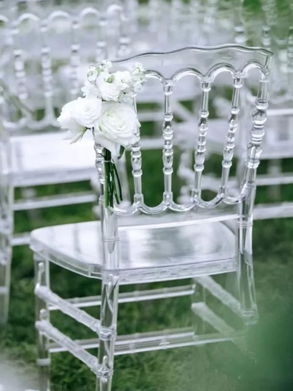 Transparent chairs decorated with white flowers for an outdoor event.