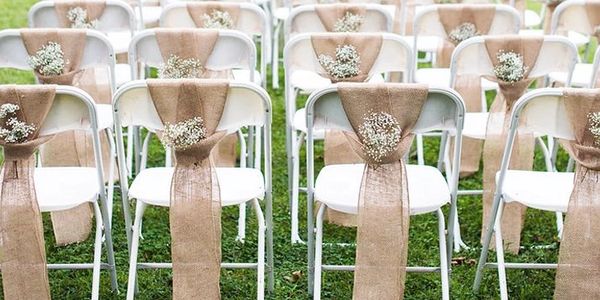 White chairs decorated with burlap and baby's breath flowers for an outdoor event.