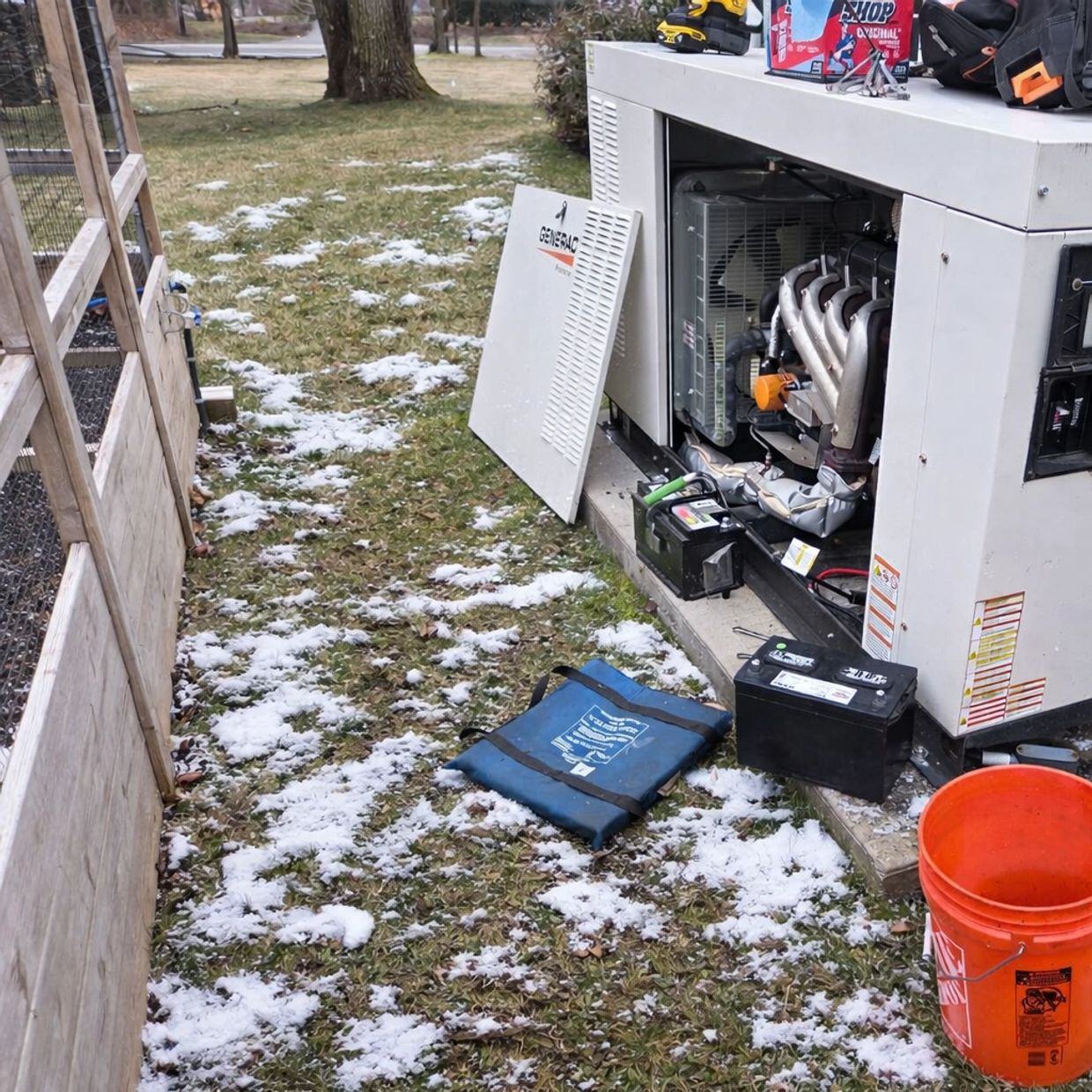 Outdoor generator with open panel and scattered snow on grass.