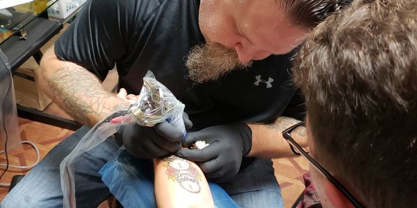 Tattoo artist working on a colorful tattoo on a client's arm.