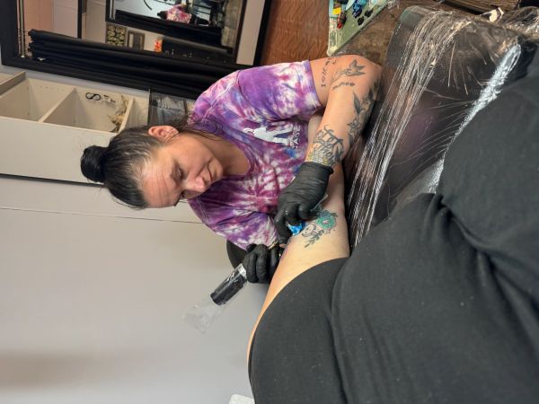 Tattoo artist working on a colorful tattoo on a client's thigh.