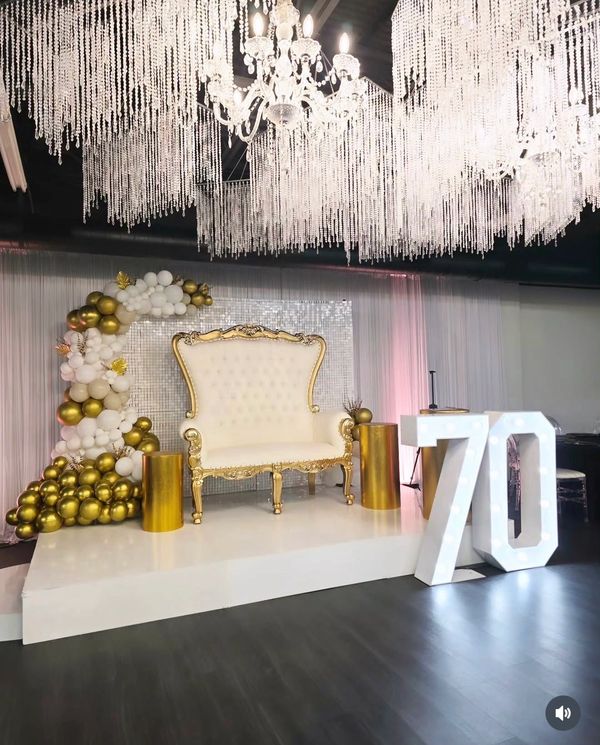 Elegant 70th birthday setup with golden balloons and chandelier.