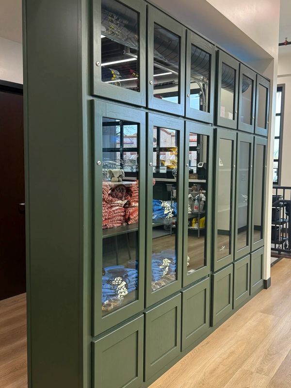 Green display cabinet with glass doors holding folded clothes.