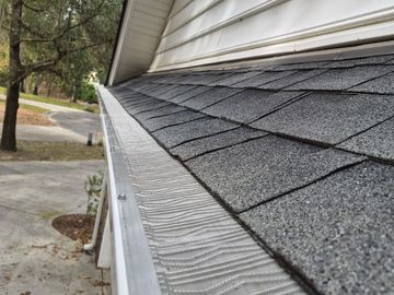 Clean gutter with leaf guard installed along asphalt shingle roof.