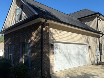 Two-story house with brick and beige siding and a white garage door under a clear blue sky.