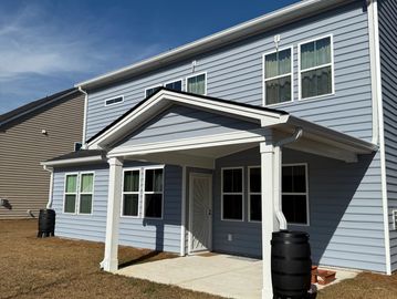 Two-story house with light blue siding and a covered patio under a clear sky.