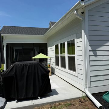 Backyard patio with grill covered in black cover beside a white house.