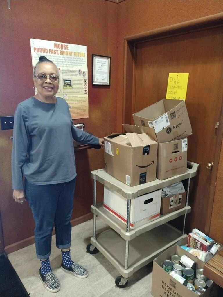 Woman standing next to a cart filled with boxes and food items.