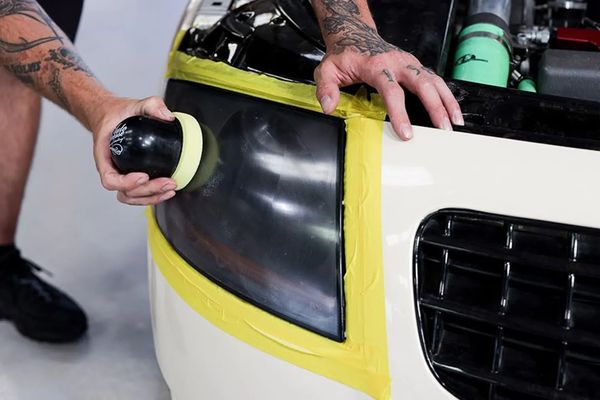 A guy using a polishing machine to buff out a headlight during a headlight restoration service