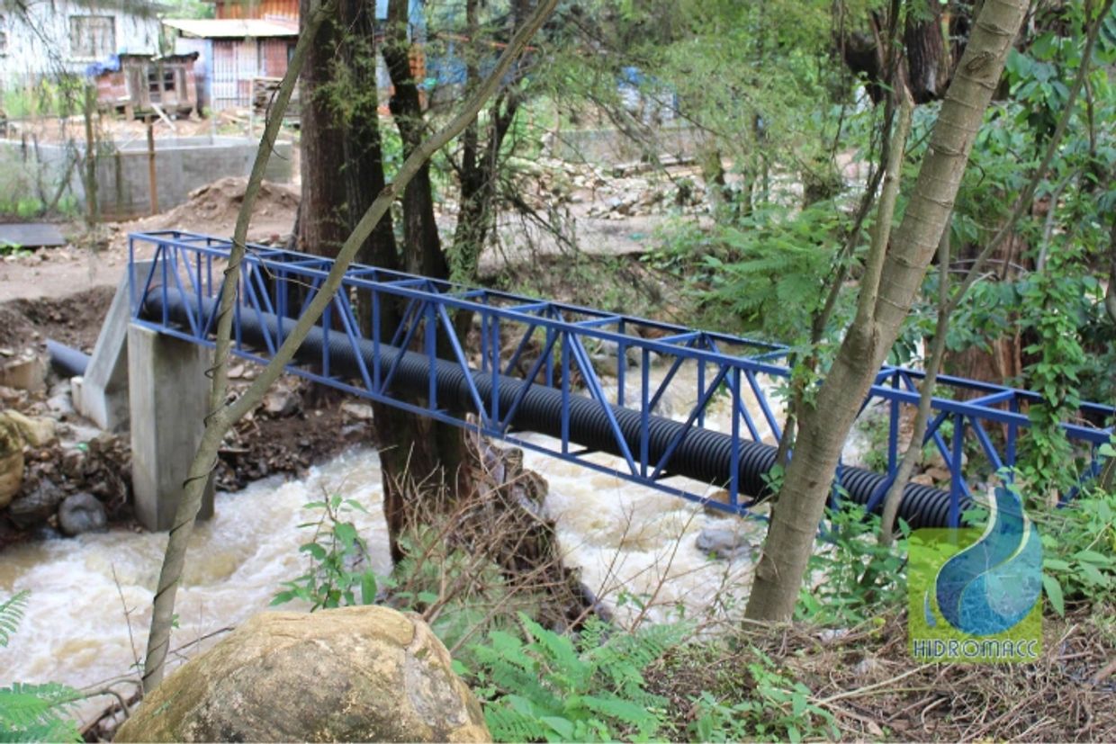 Puente metálico azul sobre un río con vegetación alrededor.