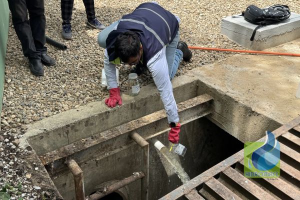 Persona recogiendo muestra de agua en una alcantarilla.