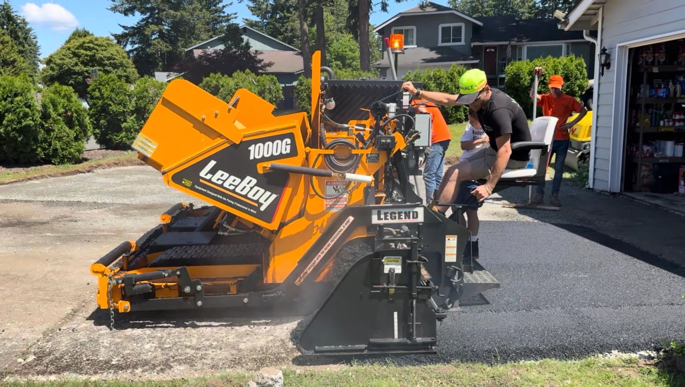 Asphalt worker laying down blacktop on a sunny day using an asphalt paver machine