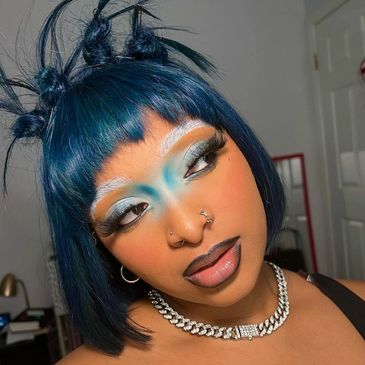 Person with bold blue makeup and styled blue hair posing indoors.