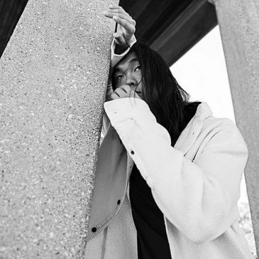 Black and white portrait of a thoughtful woman leaning on a concrete pillar.