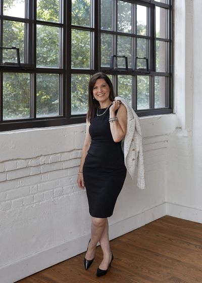 Woman in a black dress holding a jacket over shoulder.
