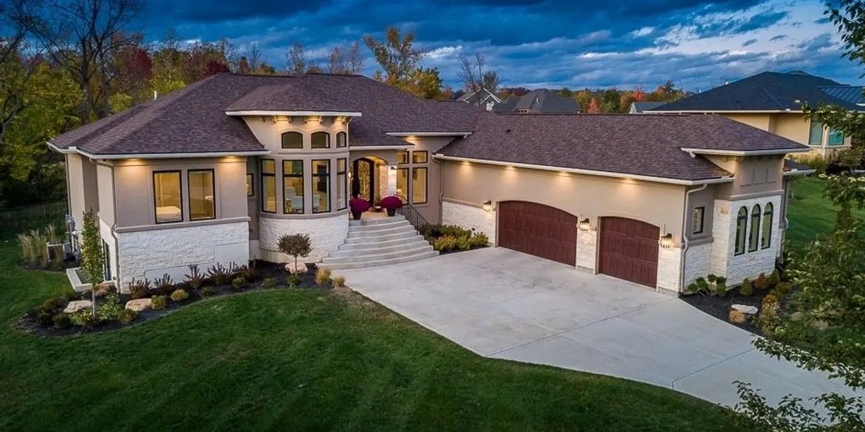 Modern single-story house with a spacious driveway and warm exterior lighting.