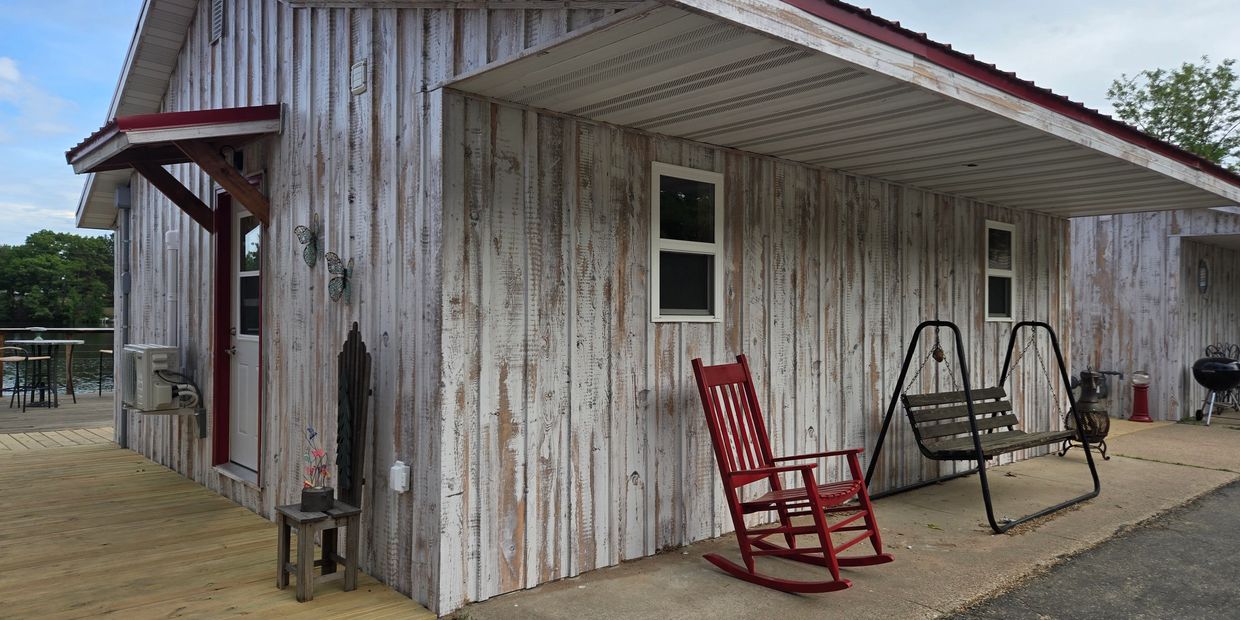 Rustic porch with a red rocking chair and swing beside a weathered wooden cabin.