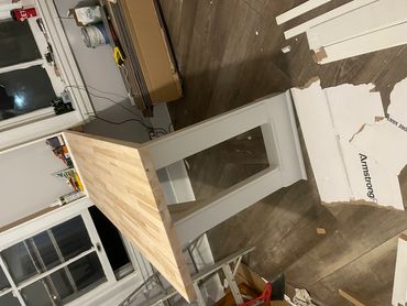 A wooden tabletop supported by a white painted base in a room under renovation.