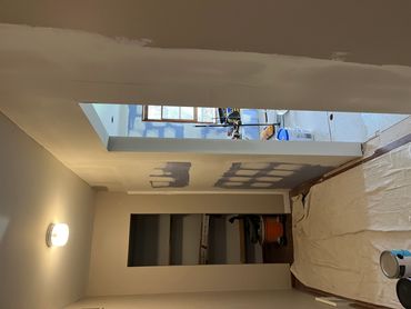 A hallway under renovation with paint supplies and patchwork walls.