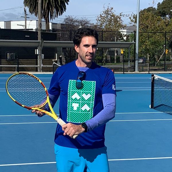 Man holding tennis racket on outdoor blue tennis court.
