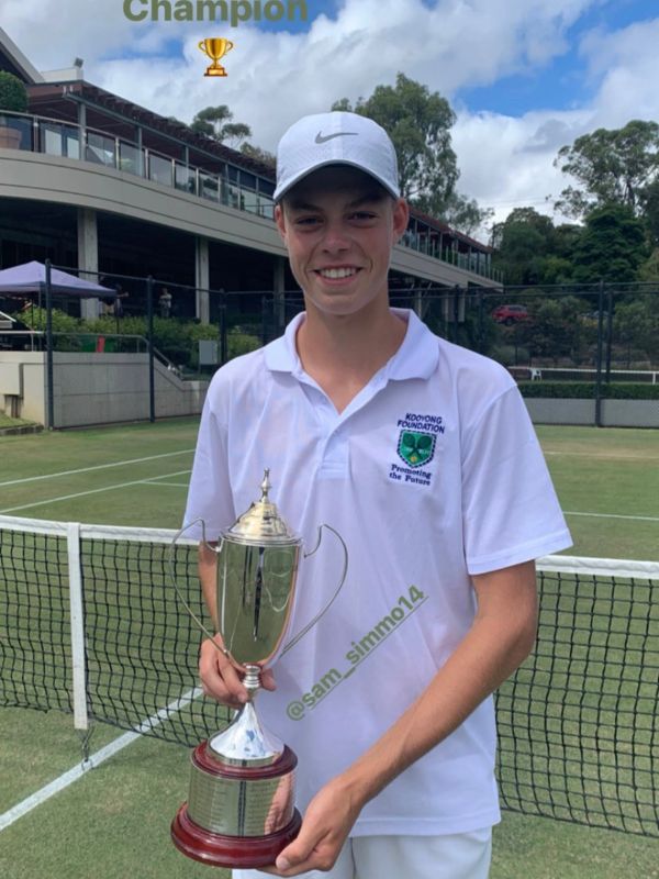 Young tennis champion holding a trophy on a grass court.