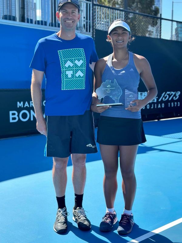 Two tennis players posing with trophies on a blue court.