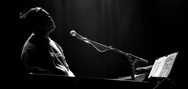 Musician playing keyboard under spotlight in black and white.