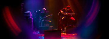 Two musicians performing on stage with colorful lighting.