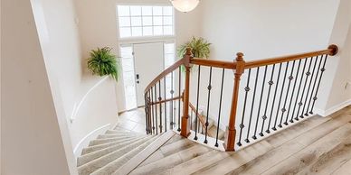 Bright staircase with wooden and iron railing and green plants near the entrance.