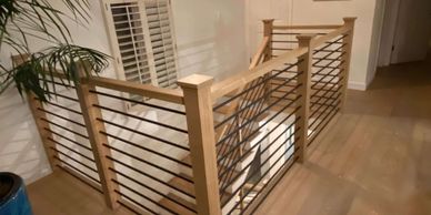 Modern wooden staircase railing with black horizontal bars in a bright room.