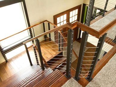 Modern wooden staircase with metal cable railing and carpeted upper floor.