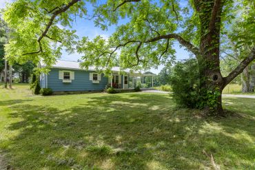 Blue house surrounded by lush green trees and grass under a sunny sky.