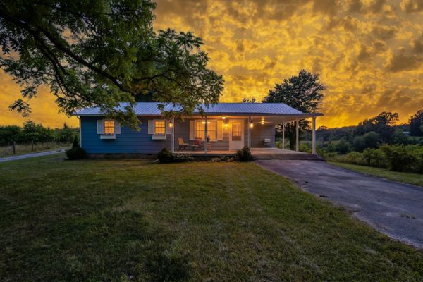 Cozy blue house at sunset with glowing windows and a dramatic sky.