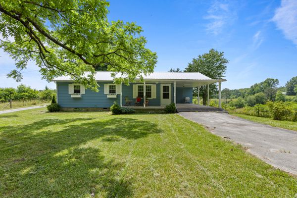 Cozy blue house with a white porch and lush green surroundings.