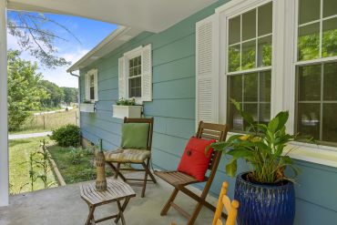 Cozy porch with wooden chairs and colorful cushions overlooking a green yard.